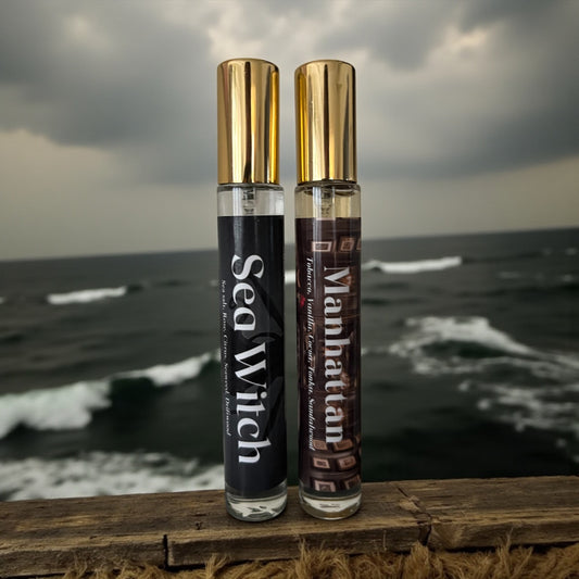 Two perfume bottles labeled 'Sea Witch' and 'Manhattan' on a wooden surface with an ocean background.