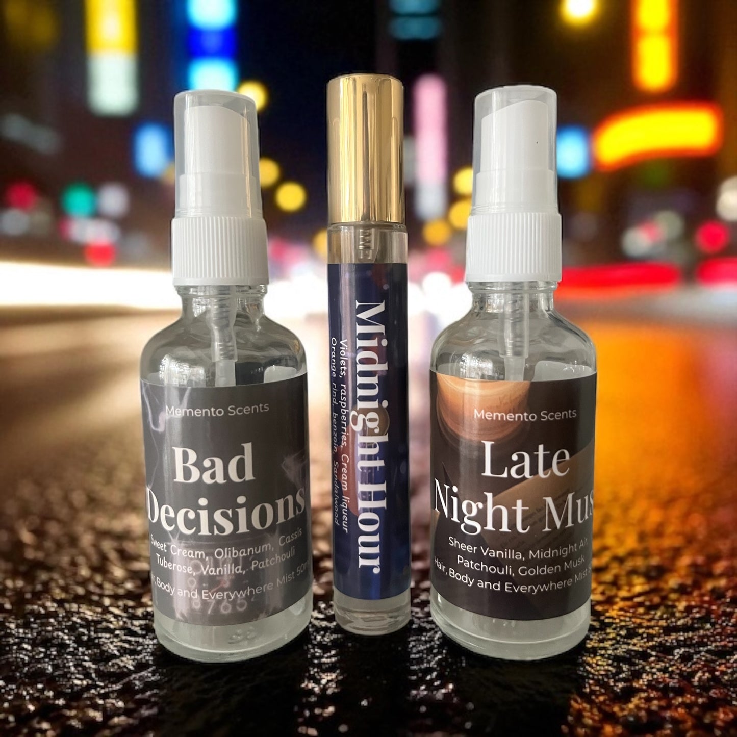 Three spray bottles labeled 'Bad Decisions', 'Midnight Hour', and 'Late Night Music' on a reflective surface with a blurred colorful background.