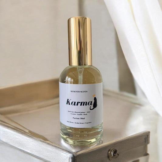 Karma perfume bottle, surrounded by elements of sun-soaked leather, roasted plums, and sweet musk, with notes of aged rum, vanilla, amber, and patchouli.