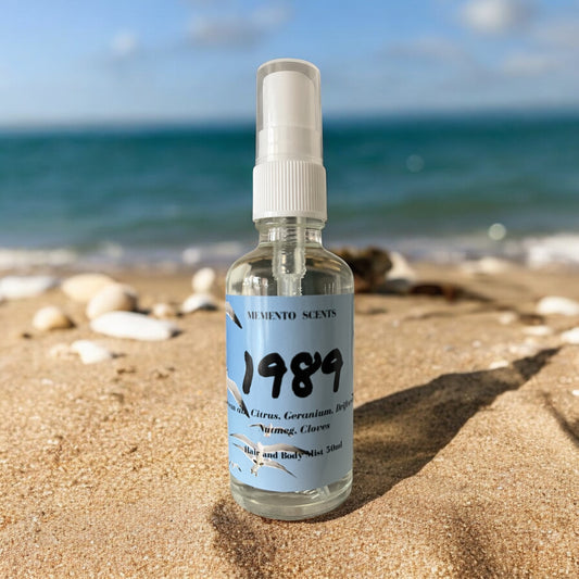 1989 a beachy citrus floral perfume  bottle on a beach in the sand with the ocean behind on a clear sunny day