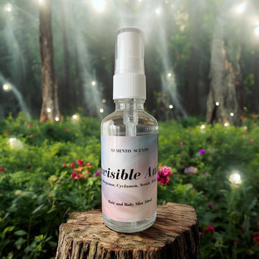 A bottle of Invisible Aura Hair and Body Mist on a tree stump with a magical forest with fairy lights and blooms in the background
