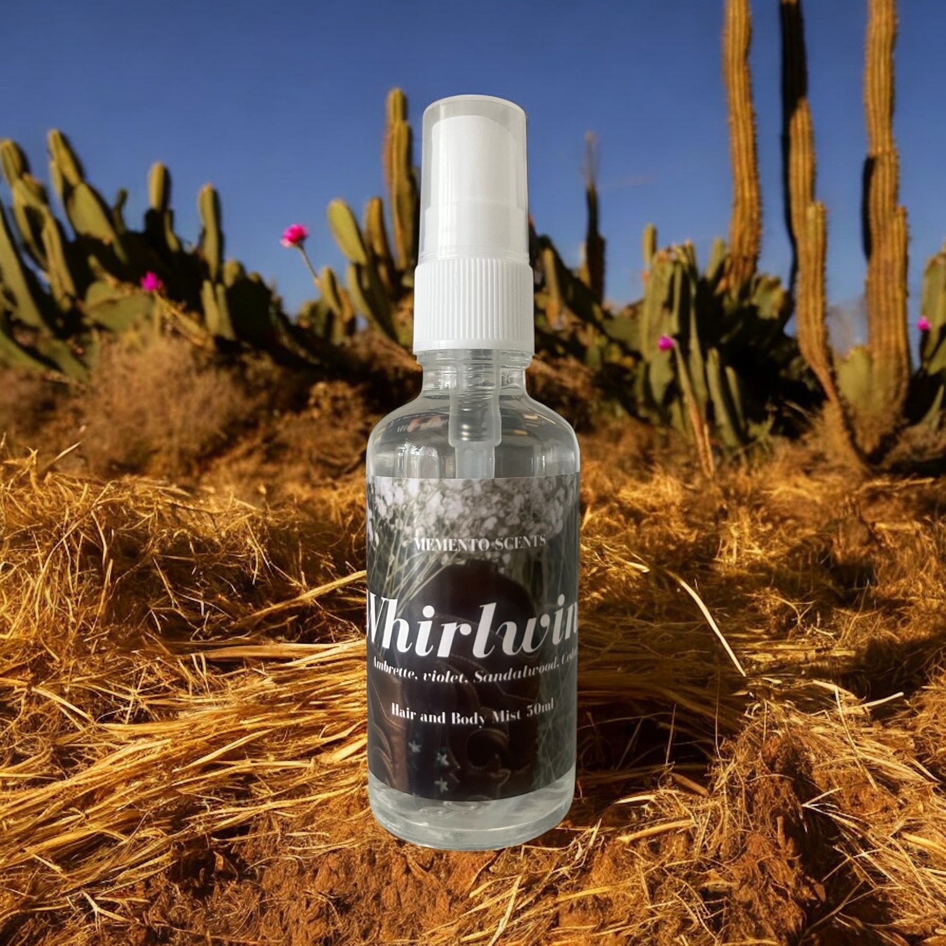A bottle of whirlwind hair and body mist on a bed of hay with cactus flowers and violets