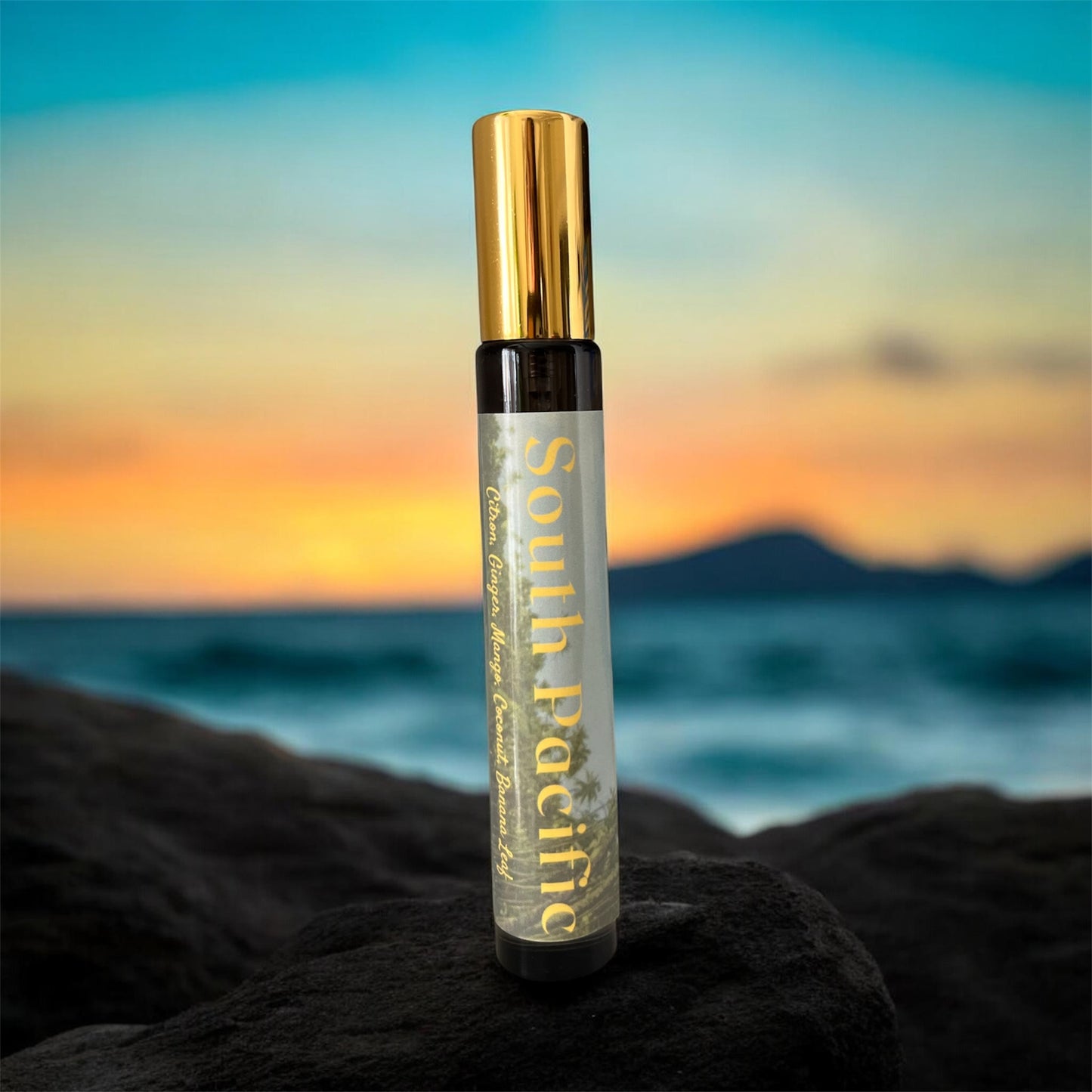 Spray bottle with gold cap and 'South Pacific' label on a rock with a sunset ocean background - Tropical Gourmand Parfum