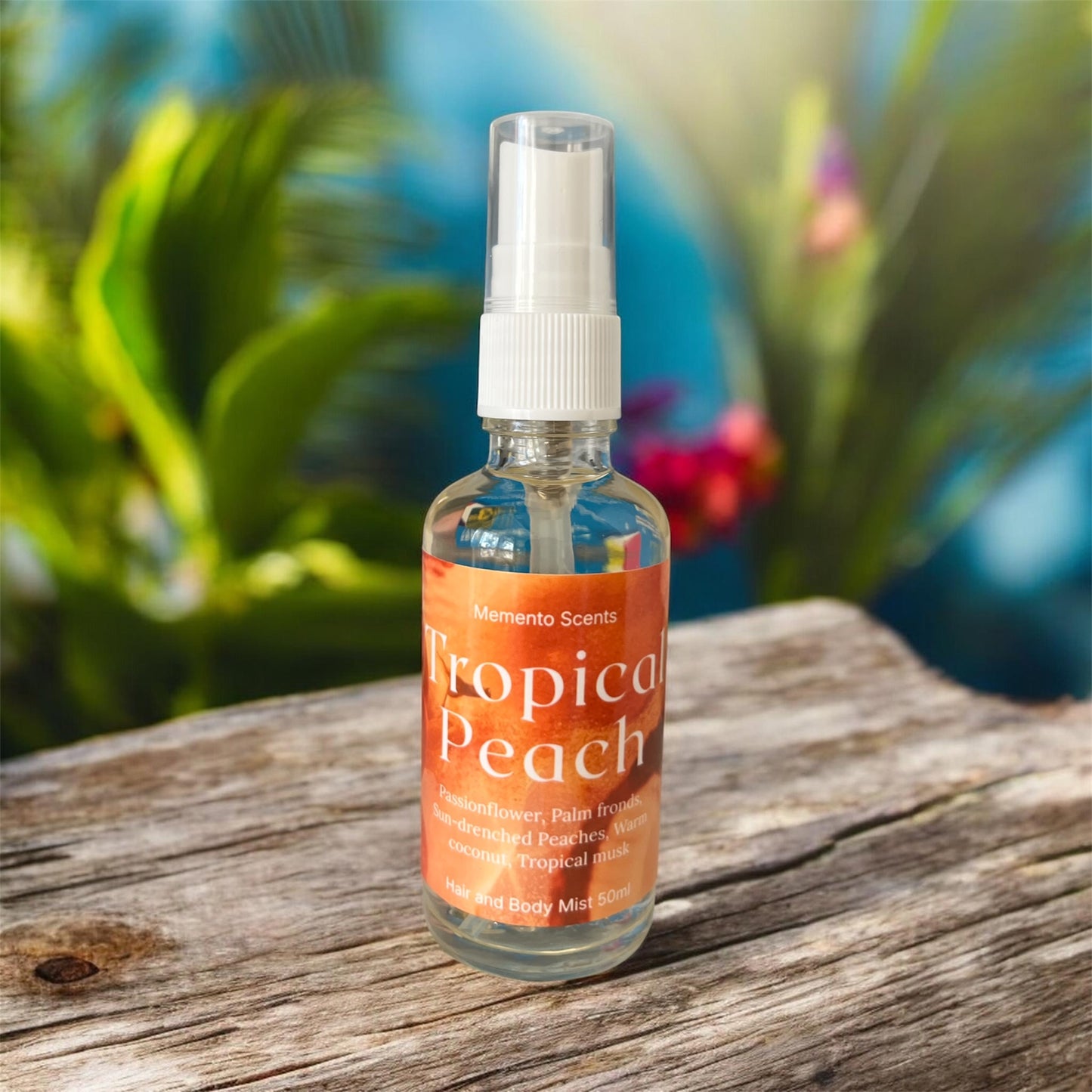 A glass spray bottle of hair and body mist named Tropical Peach on a raw wooden table with a lush tropical background