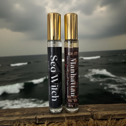 Two perfume bottles labeled 'Sea Witch' and 'Manhattan' on a wooden surface with an ocean background.