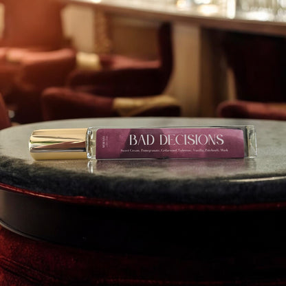 Bad Decisions perfume bottle, surrounded by bold, chaotic elements with notes of cassis, jasmine, tuberose, vanilla, and olibanum.