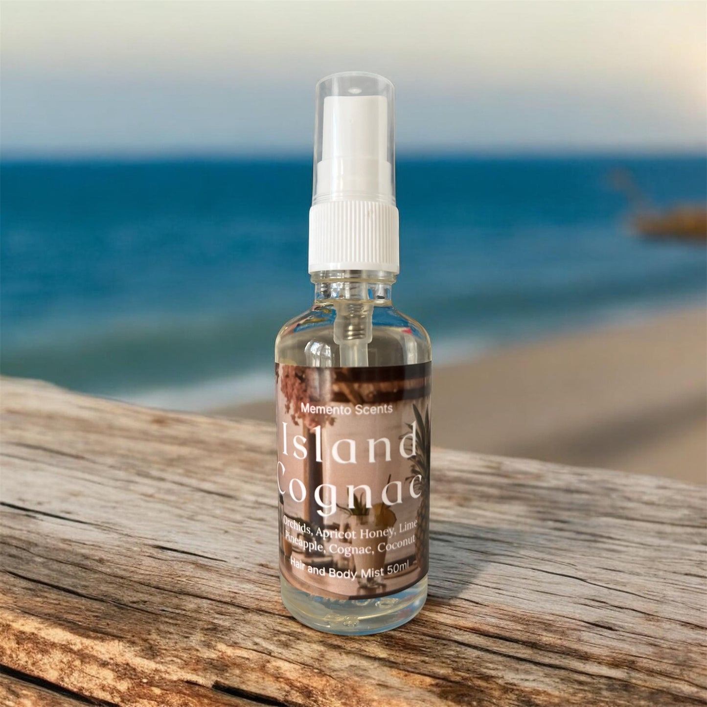 A glass spray bottle of hair and body mist on a wood ledge with the ocean behind named Island Cognac
