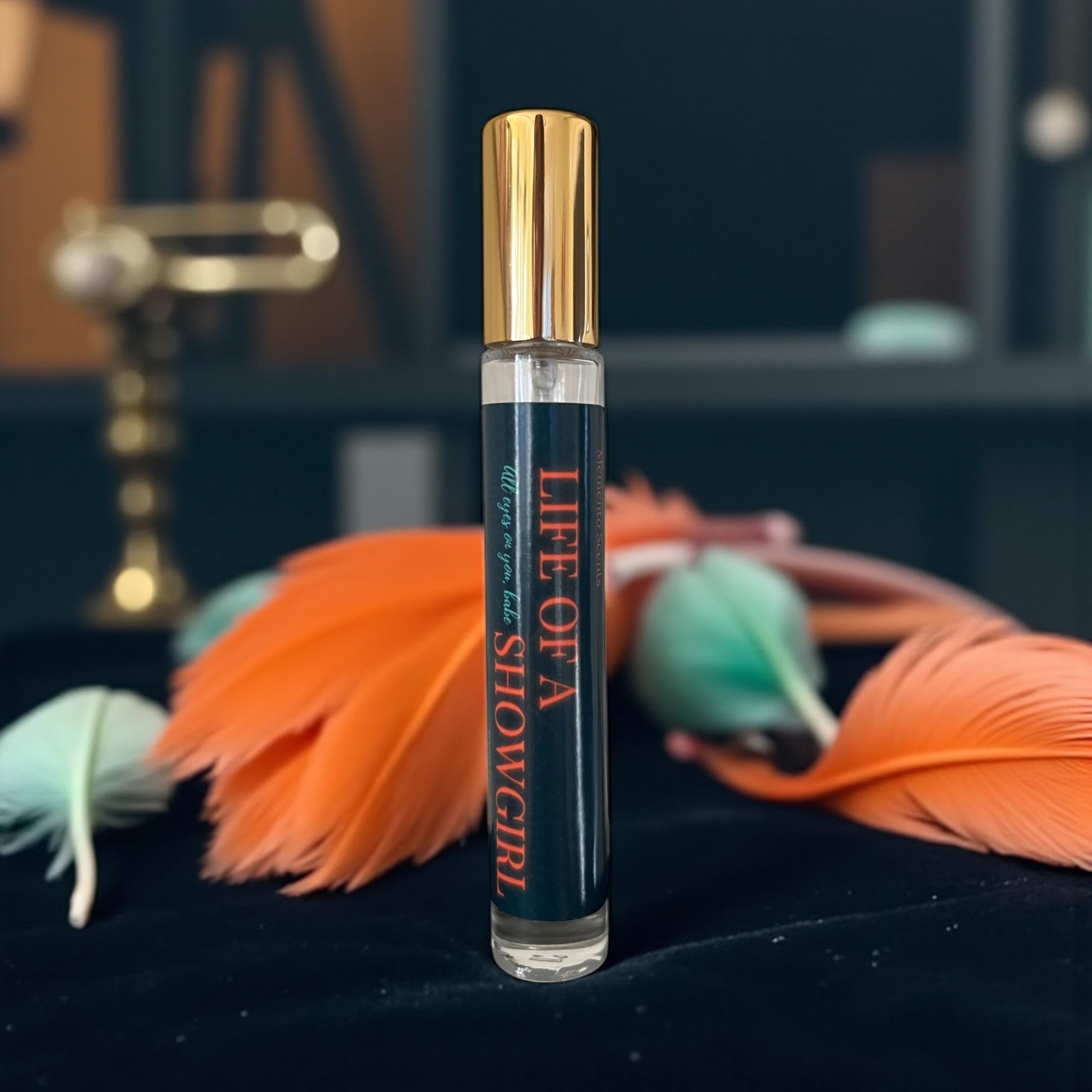 A bottle of perfume labelled Life of a Showgirl with orange and mint feathers on a table