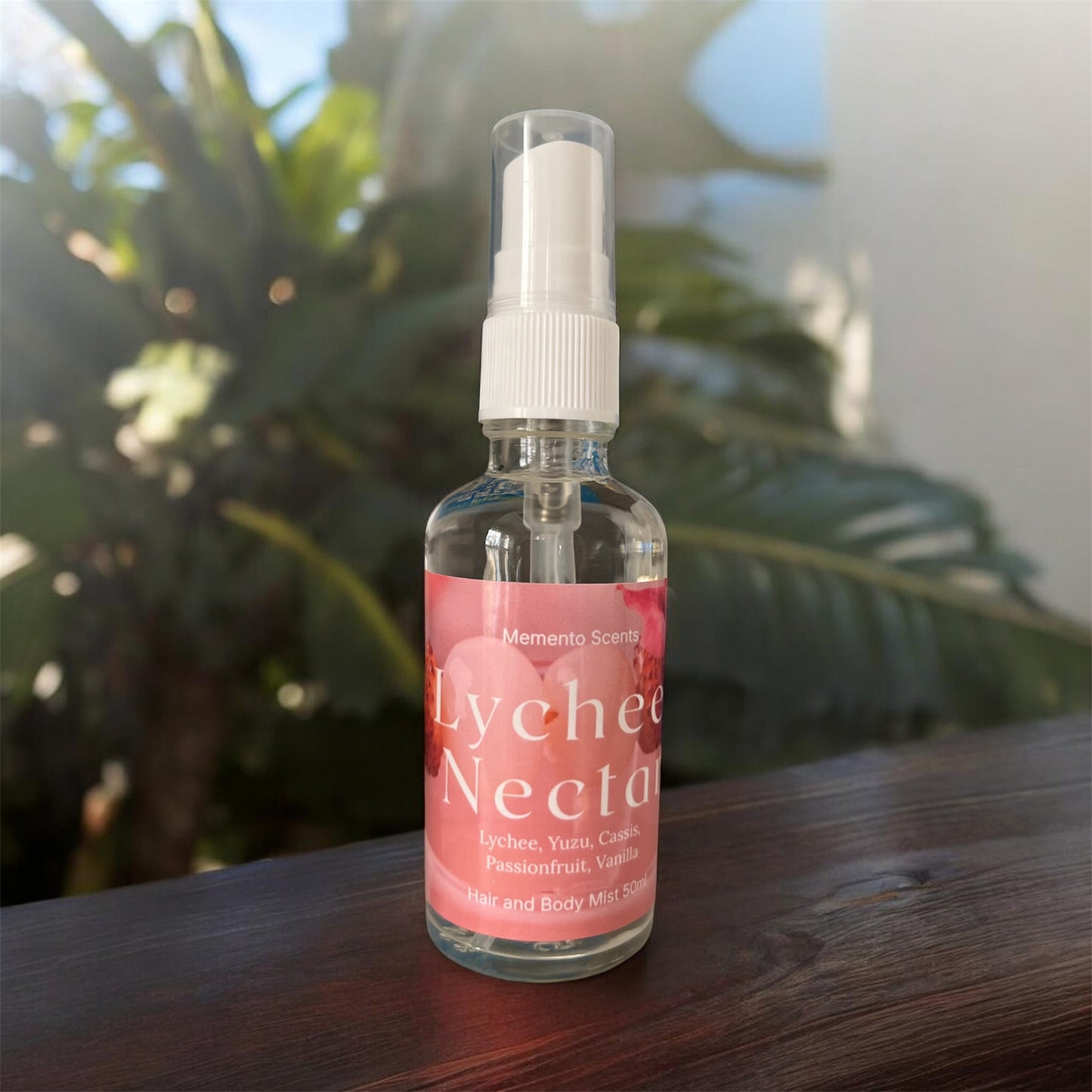 A spray bottle of Lychee Nectar Hair and body mist on a wood surface surrounded by lush foliage
