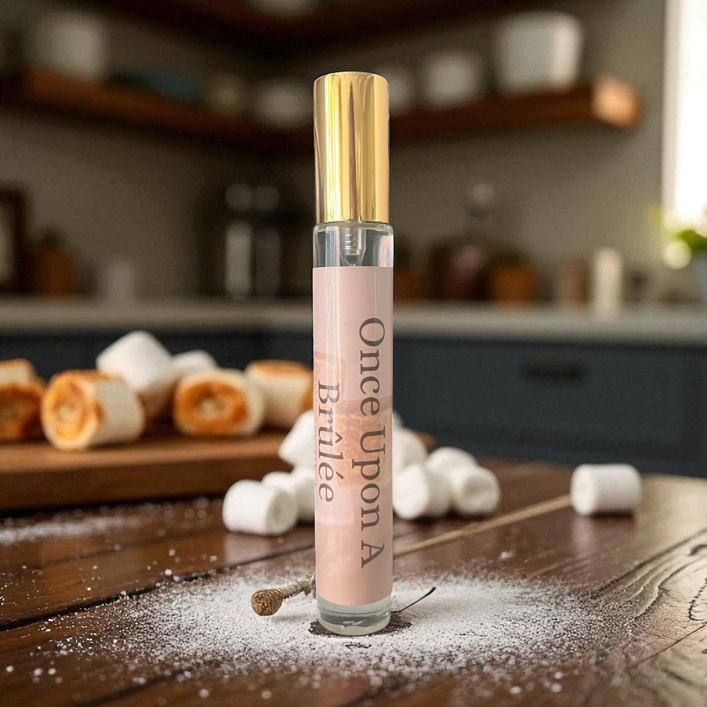Perfume bottle labeled 'Once Upon A Brulée' on a wooden surface with marshmallows and a blurred kitchen background.