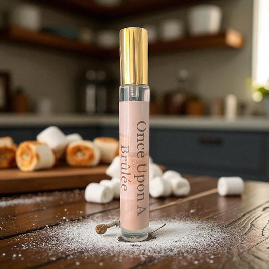 Perfume bottle labeled 'Once Upon A Brulée' on a wooden surface with marshmallows and a blurred kitchen background.