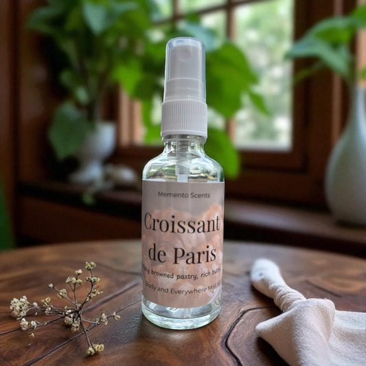 Bottle of 'Croissant de Paris' scented spray on a wooden surface with plants in the background