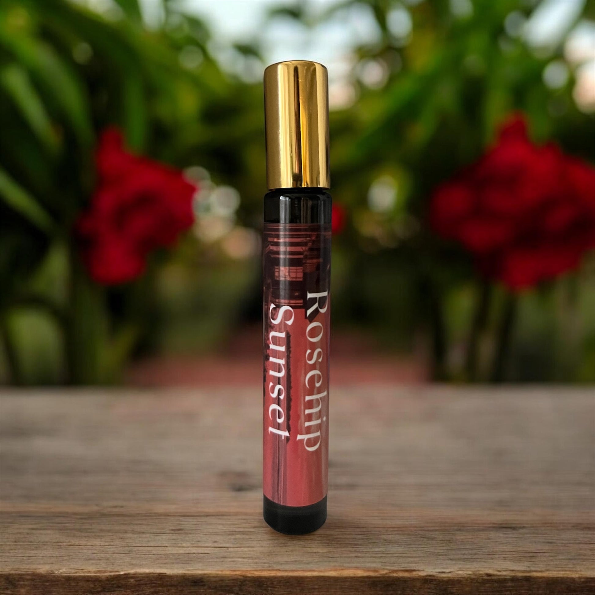Spray Glass bottle labeled 'Rosehip Sunset' on a wooden surface with blurred red flowers in the background