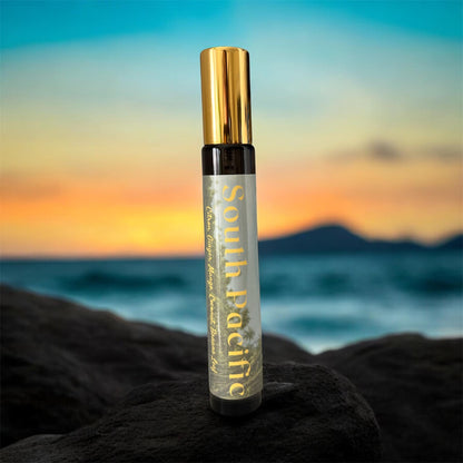 Spray bottle with gold cap and 'South Pacific' label on a rock with a sunset ocean background - Tropical Gourmand Parfum