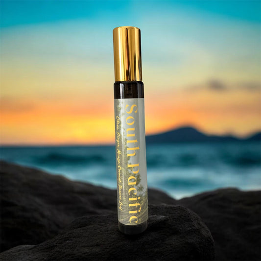 Spray bottle with gold cap and 'South Pacific' label on a rock with a sunset ocean background - Tropical Gourmand Parfum