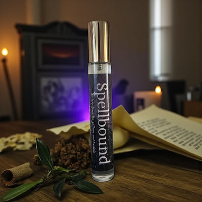 bottle of perfume labeled 'Spellbound' on a wooden surface with herbs and candles in the background