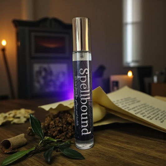 bottle of perfume labeled 'Spellbound' on a wooden surface with herbs and candles in the background
