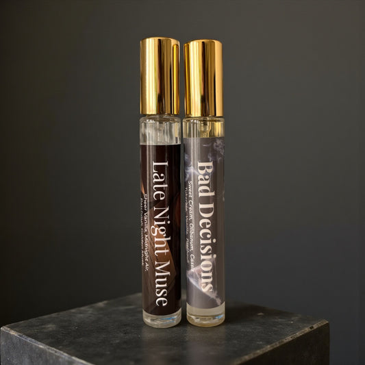 Two perfume bottles labeled 'Late Night Muse' and 'Bad Decisions' on a dark surface with a dark background.