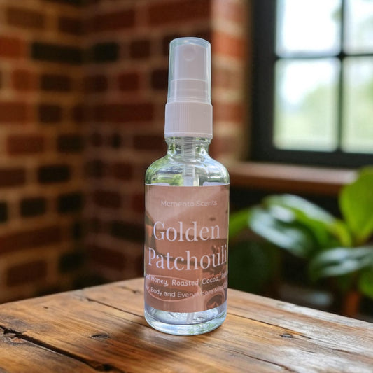 Bottle of Golden Patchouli  body spray on a wooden surface with a brick wall and plant in the background